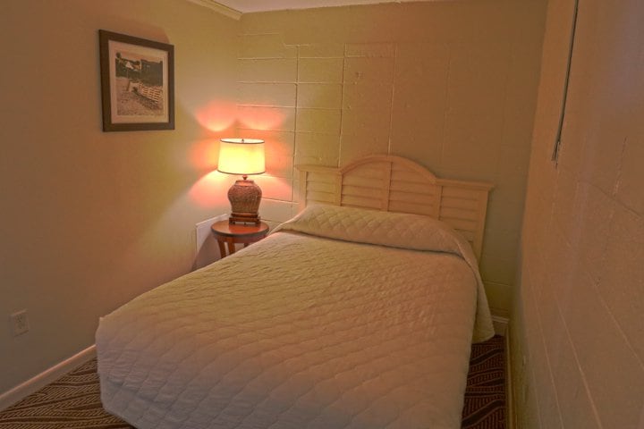 A small hotel room with a single bed, nightstand, and lamp.