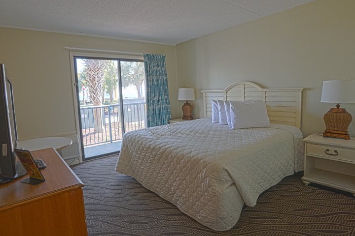 A hotel room with a bed, nightstands, a TV, and a sliding door leading to a balcony.
