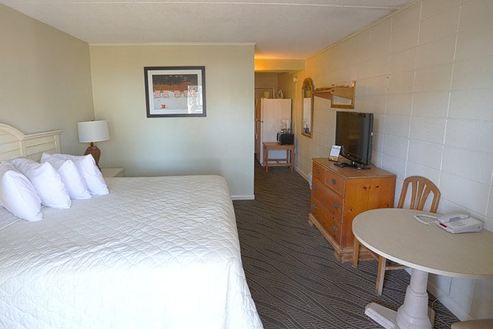 A wide view of a hotel room with a bed, TV, table, chair, and dresser.