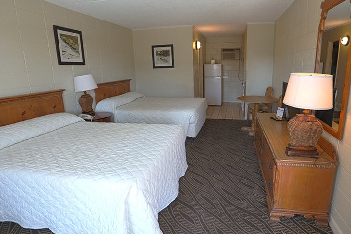 A hotel room with two beds, a desk, and a kitchenette.