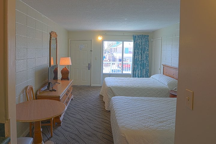 A hotel room with two beds, a window, and a desk.