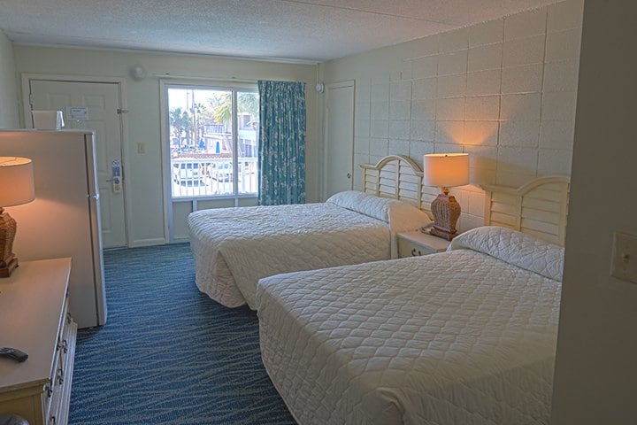 A hotel room with two beds, blue carpet, and white walls.