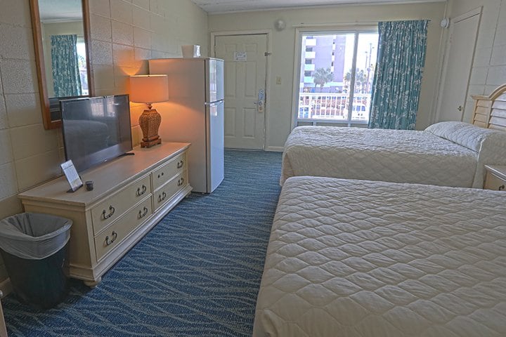 A hotel room with two beds, a refrigerator, and a TV.