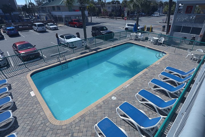 A rectangular outdoor pool with blue lounge chairs and a fenced-in area.