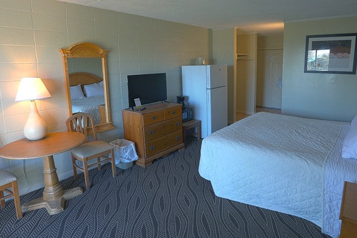 A hotel room with a bed, TV, fridge, and sitting area.