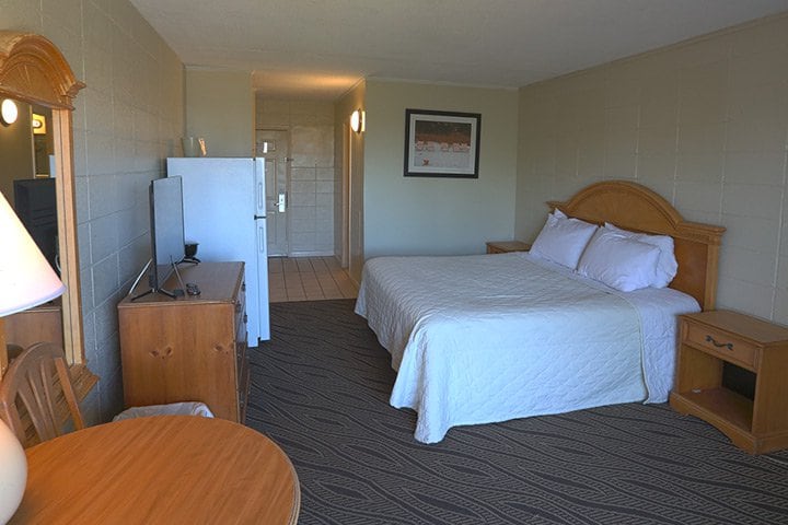 A wide view of a hotel room with a bed, desk, refrigerator, and TV.