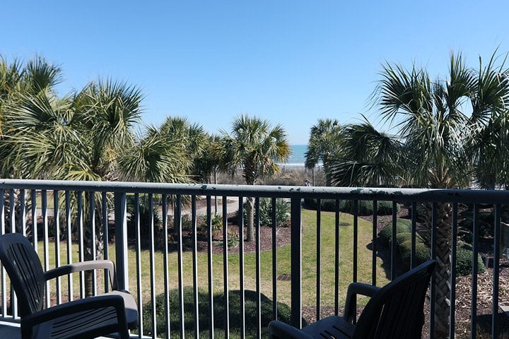 A balcony with a view of palm trees and the ocean.